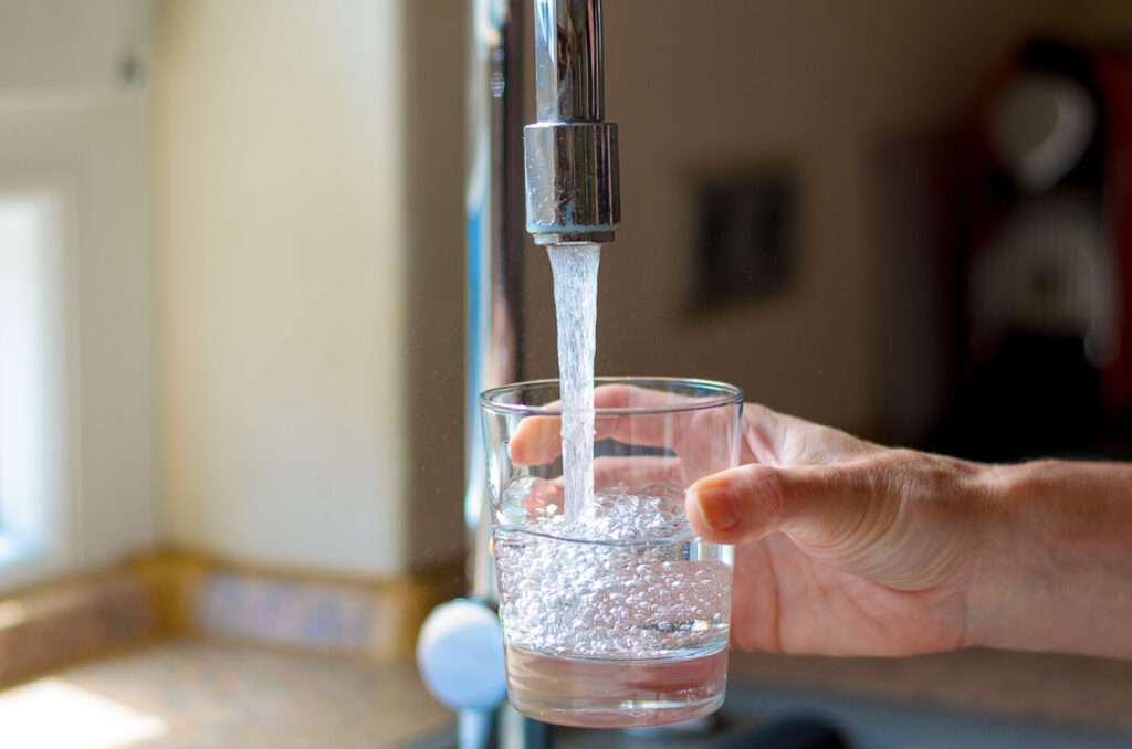 person filling up a glass of water from a tap